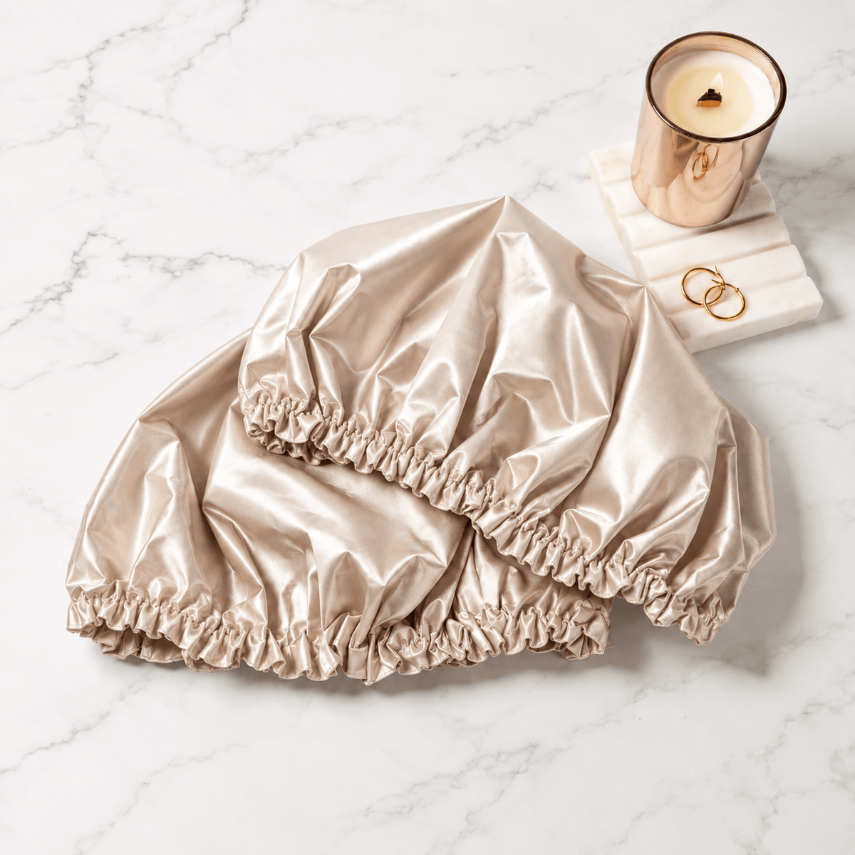 Two champagne satin shower caps on a marble surface