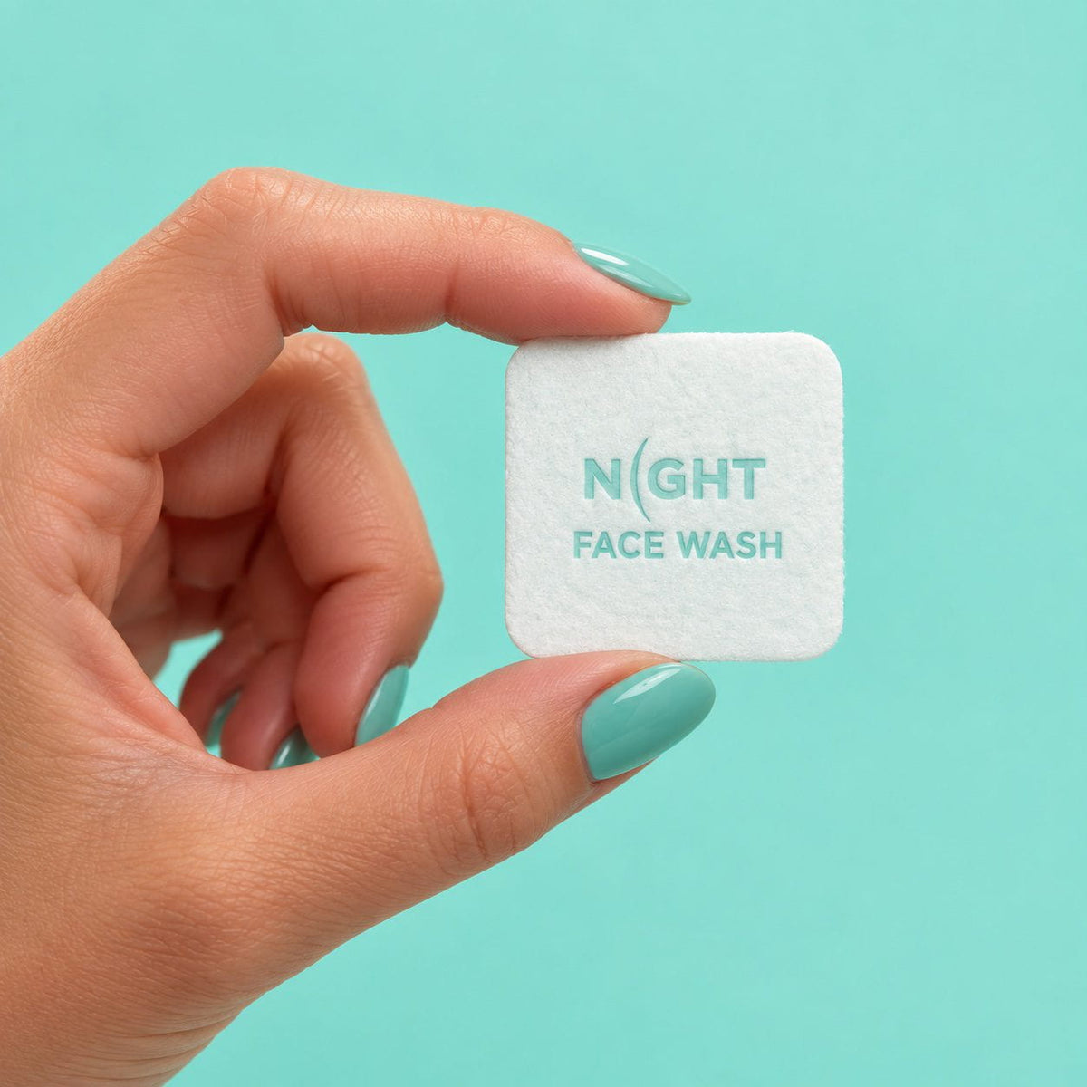 Hand with aqua nails holding one NIGHT Face Wash cleansing dose against an aqua background