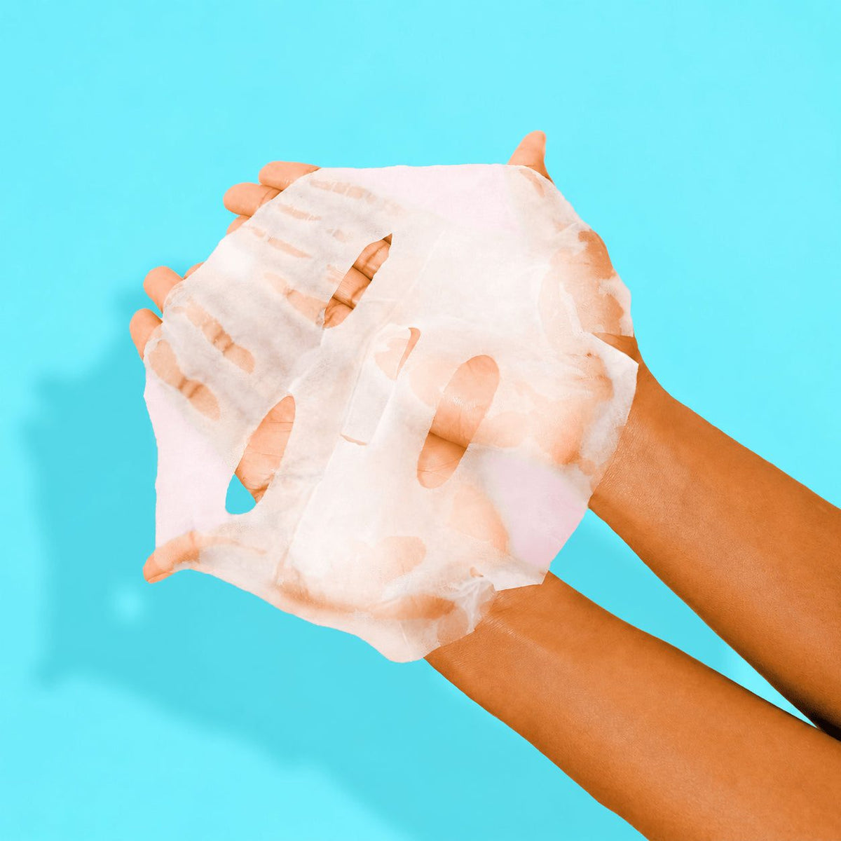 Hands holding an unfolded NIGHT hyaluronic acid sheet mask against an aqua background