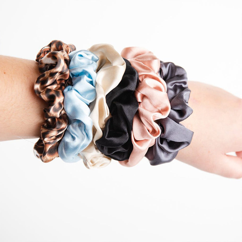 woman's arm with gunmetal, blush, black, champagne, sky and leopard colored silk scrunchies