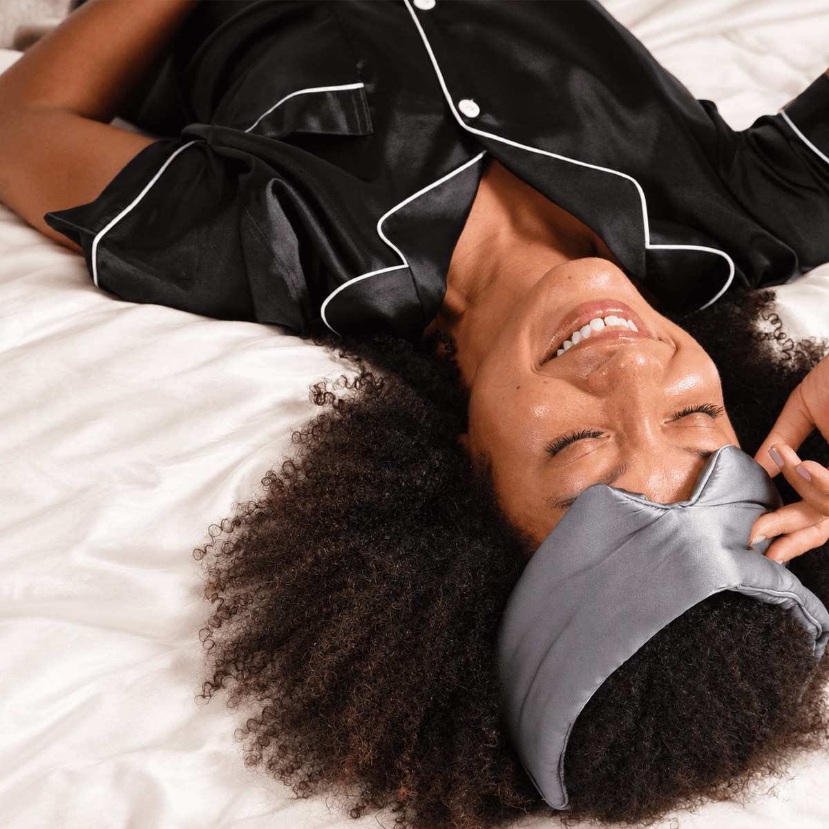 Woman relaxing in bed with the oversized gunmetal NIGHT eye mask