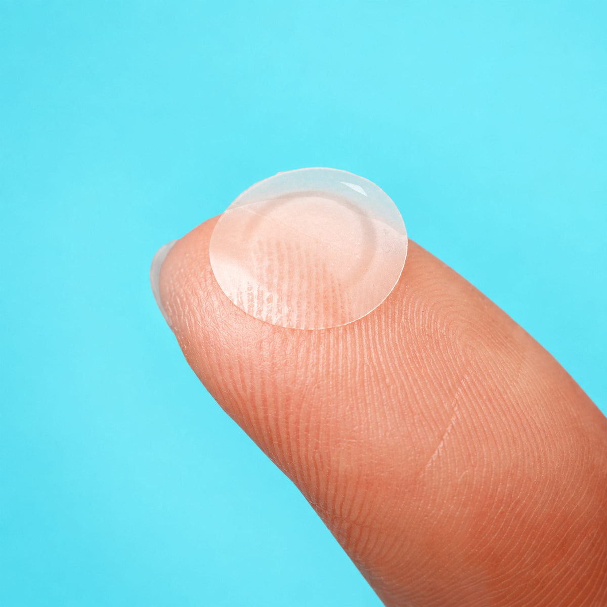 Close-up of a thin, translucent NIGHT everyday pimple patch on a fingertip