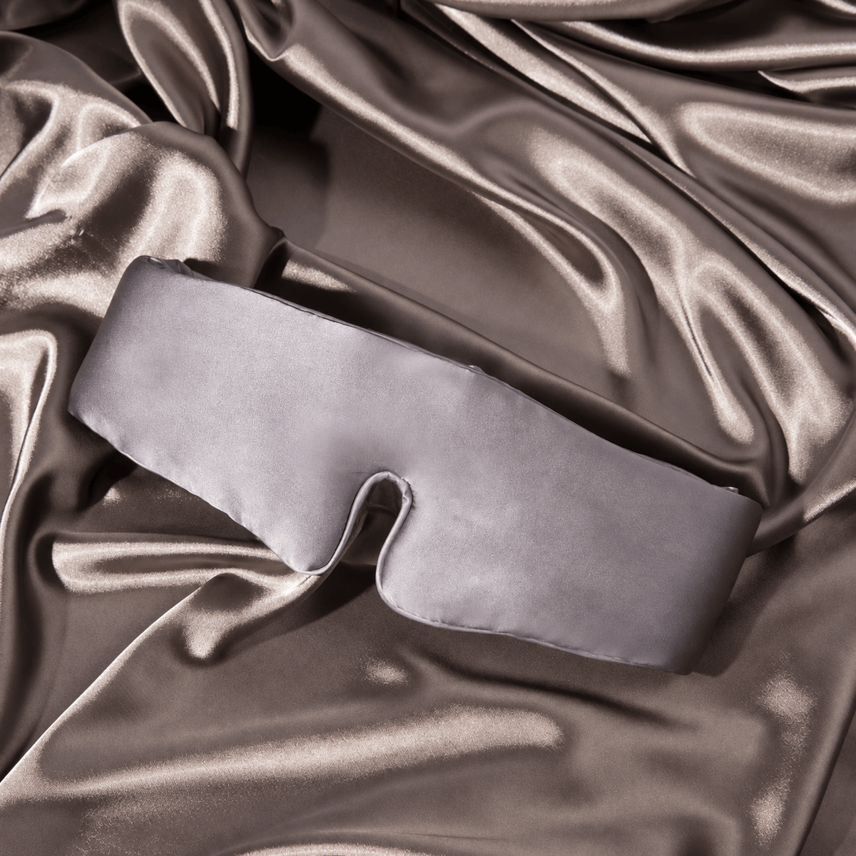 Gunmetal oversized silk sleep mask resting on softly draped fabric