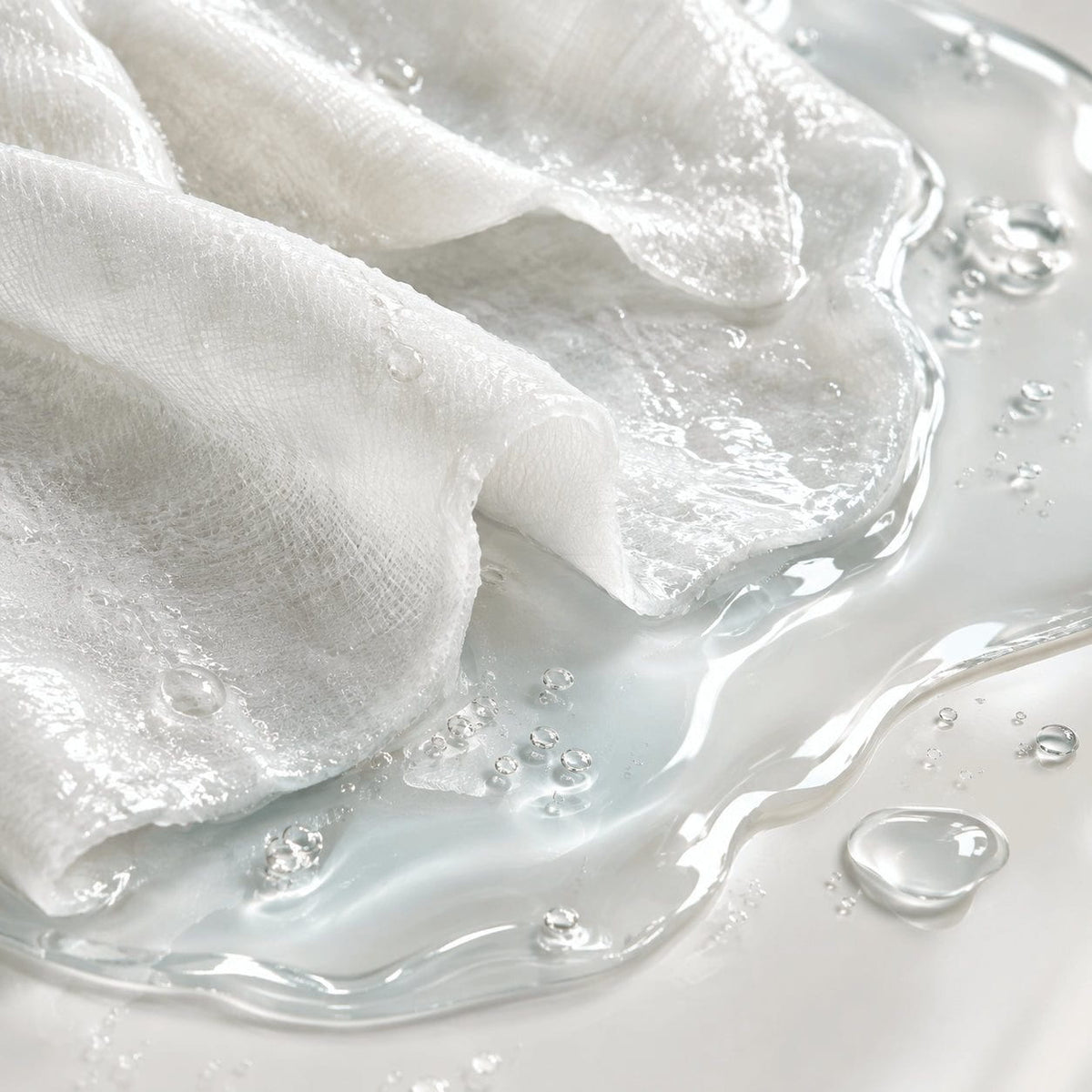Close-up of NIGHT sheet mask fabric soaked in serum, with droplets on a pale aqua surface