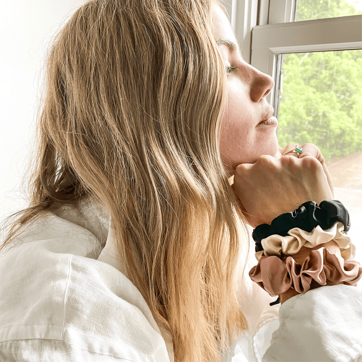 Satin scrunchies worn on a wrist beside a window