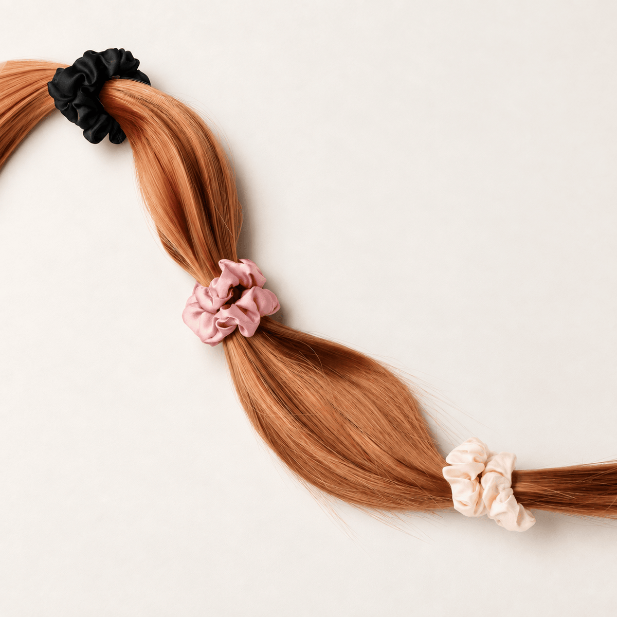 Black, Blush and Champagne Skinny silk scrunchies shown securing a hair swatch