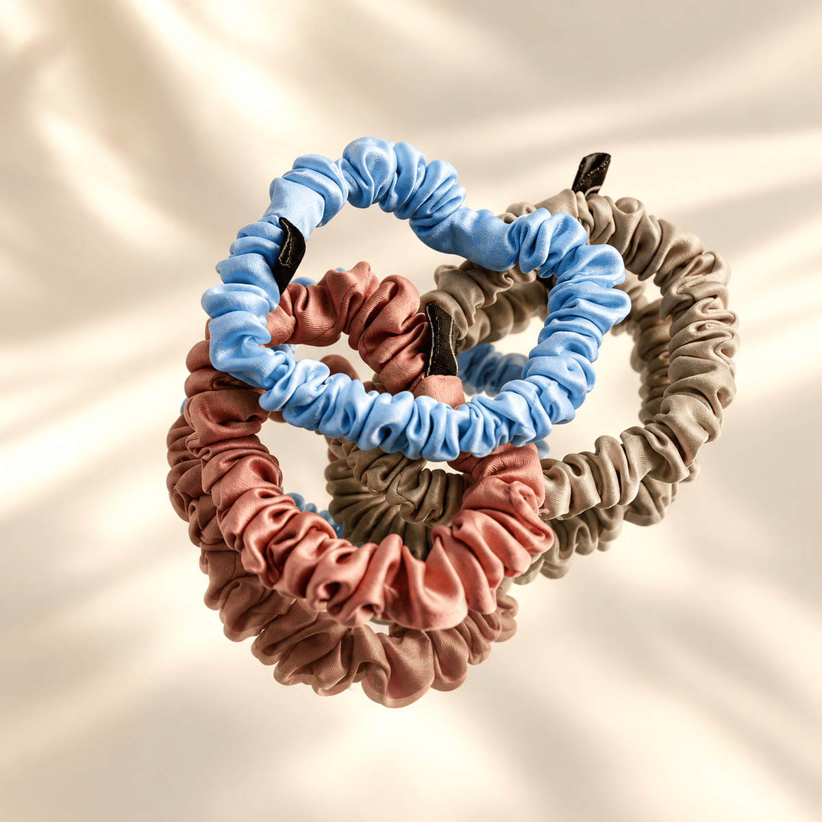 Three skinny silk scrunchies on a mirror with a warm ivory background