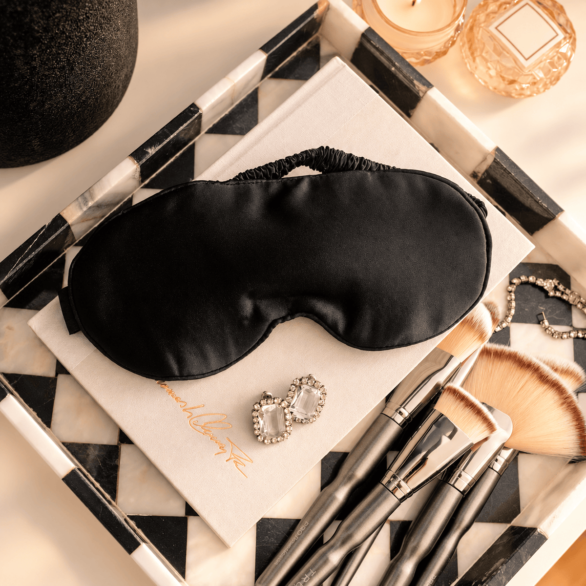 Black satin sleep mask resting on a tray beside beauty essentials