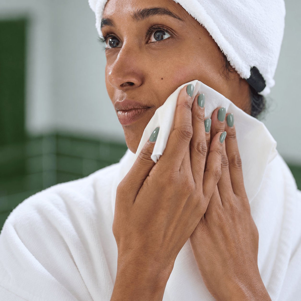 Woman with sage green nails cleansing her cheek with the NIGHT raw silk washcloth.