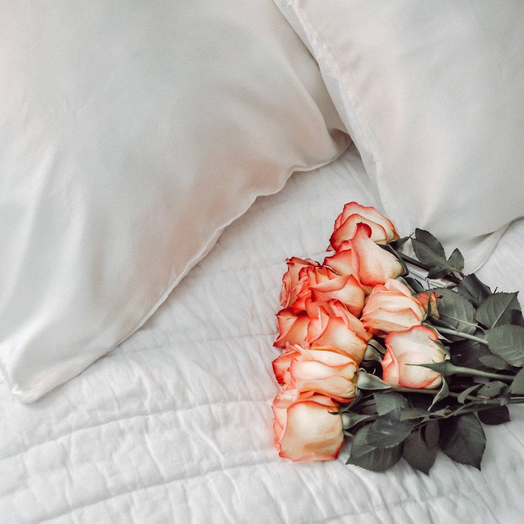roses laying on bed with clean silk pillowcase in white on pillow